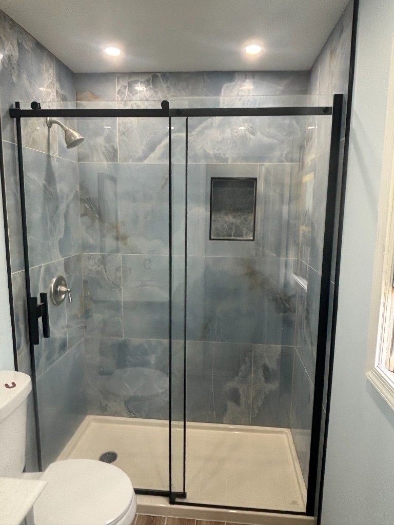 Finished marble-look walk-in shower with black sliding glass