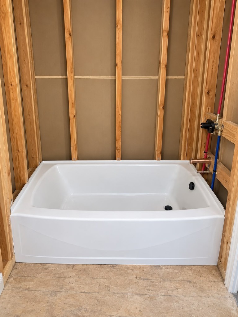 White bathtub set in a wood-framed alcove with rough plumbing
